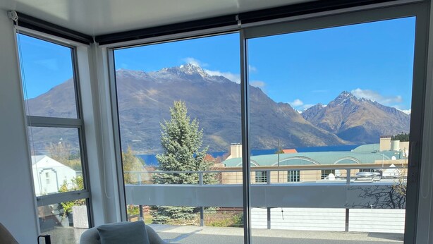 Quarto com uma cama grande, uma cadeira e vista para montanhas através de amplas janelas.
