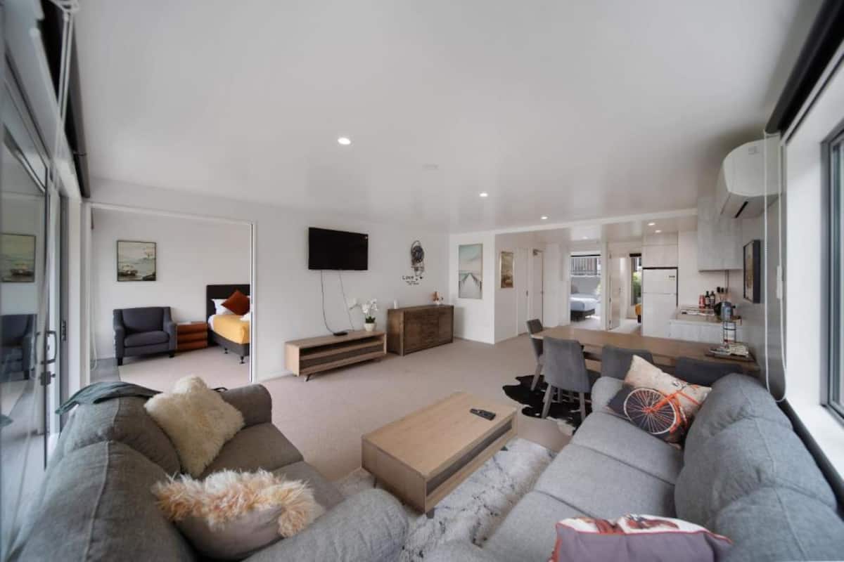 A modern living room with a grey sofa, a wooden coffee table, and a TV mounted on the wall.