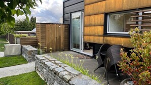 Uma casa moderna com parede de pedra, deck de madeira e um pátio com mobiliário externo.