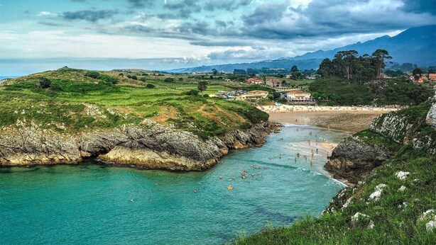 A coastal landscape with a beach, rocky cliffs, and a small settlement in the background. - Poo de Llanes House close to the Beach - El Balandro (Poo De Llanes)