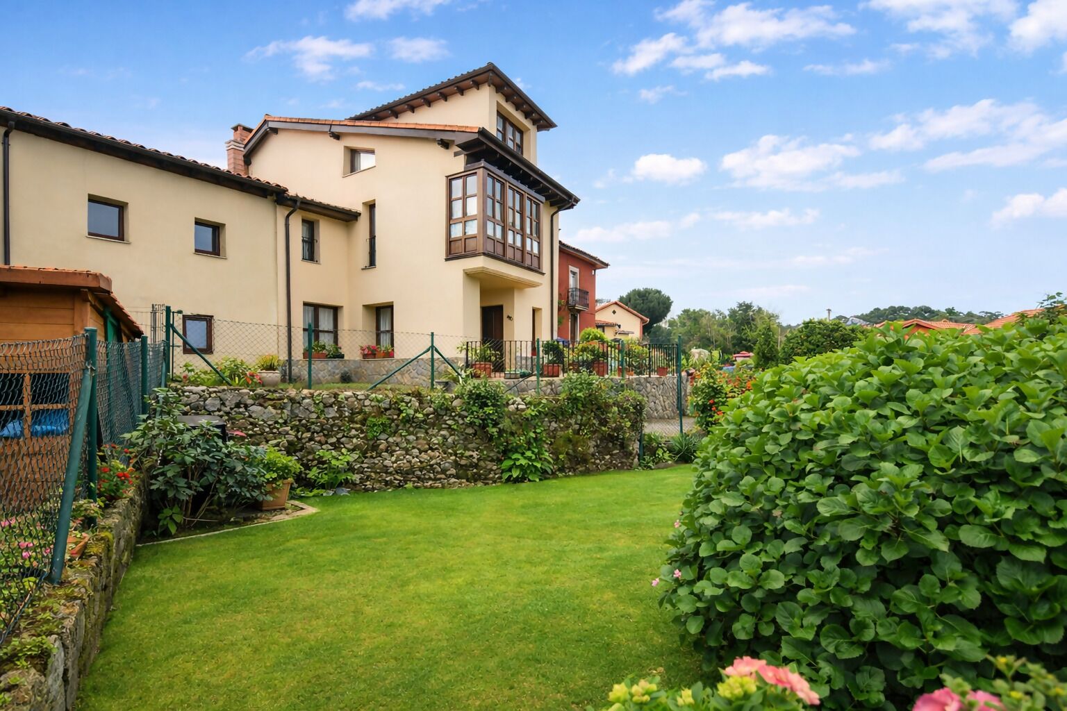 A two-story house with a stone wall and a well-maintained garden.