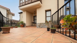 A courtyard with tiled flooring, potted plants, a stone wall, and a black railing. - Poo de Llanes House close to the Beach - El Balandro (Poo De Llanes)