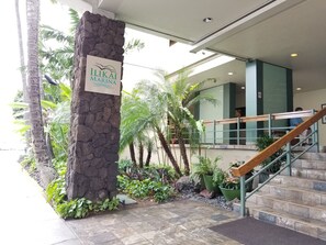 Un pilar de piedra con un cartel que dice "ILIKAI MARINA" en un vestíbulo con escaleras, palmeras y plantas de interior.