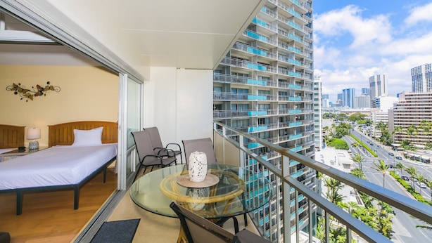 A balcony with a bed, a glass table, and chairs. - Nicely Appointed One Bedroom! City Lights and Mountain Views! (Honolulu)