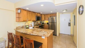 A modern kitchen with granite countertops, wooden cabinets, stainless steel appliances, and a built-in island with seating. - Nicely Appointed One Bedroom! City Lights and Mountain Views! (Honolulu)