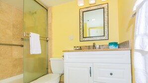 A bathroom with a glass shower enclosure, a white toilet, and a vanity with a mirror. - Nicely Appointed One Bedroom! City Lights and Mountain Views! (Honolulu)