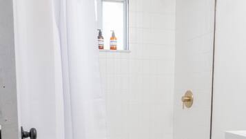 A bathroom with a shower, toilet, and a window.