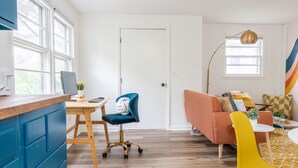 Een moderne woonkamer met een houten vloer, een blauwe stoel, een gele stoel, een bank en een bureau met een computer.
