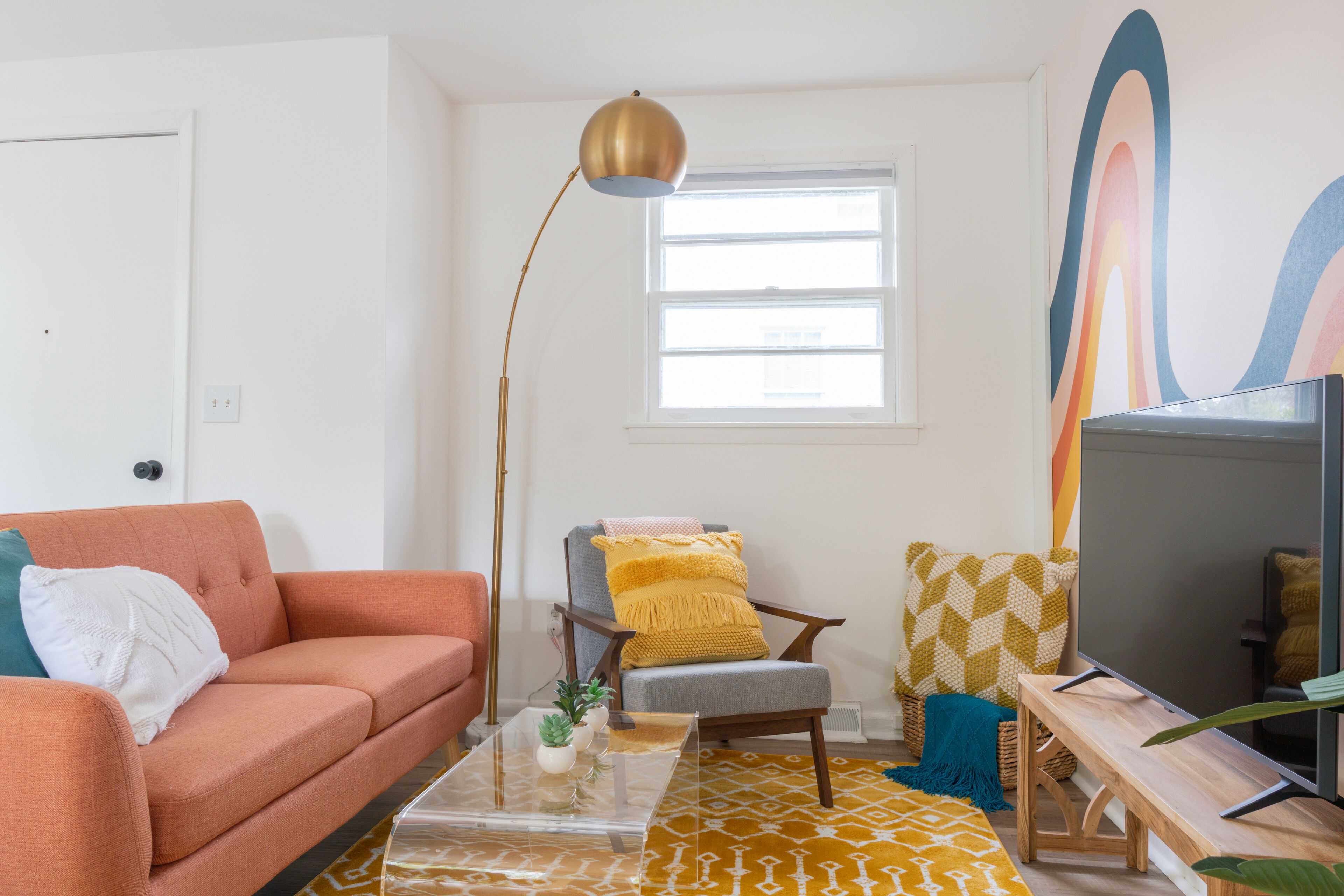 A living room with a sofa, armchair, coffee table, floor lamp, and a television.