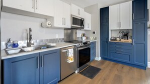 Una cucina moderna con mobili bianchi e blu, elettrodomestici in acciaio inox e pavimento in legno.