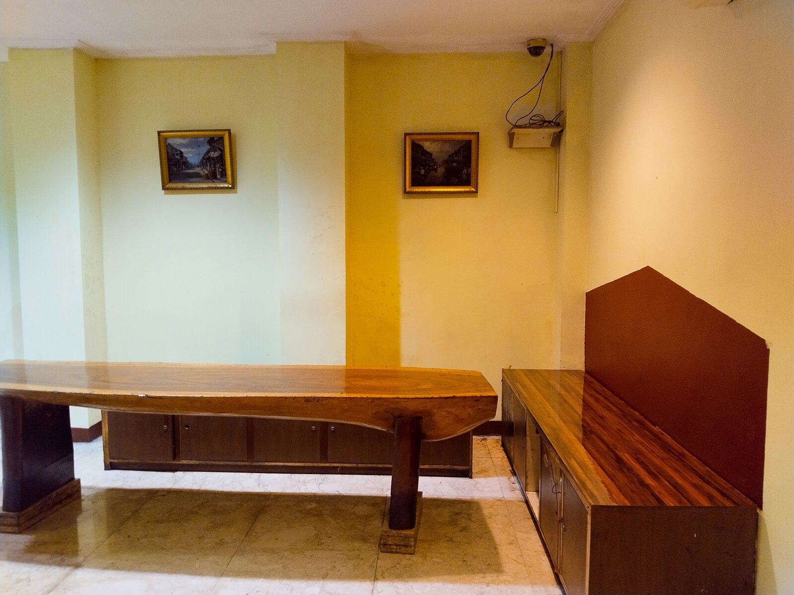 Una habitación con una larga mesa de madera, un banco y dos cuadros en las paredes.