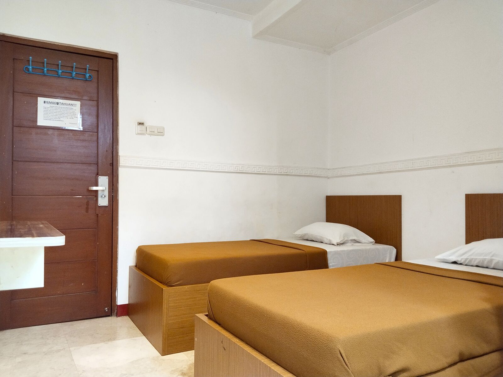 A room with two single beds, a wooden door with a coat rack, and a small white table.