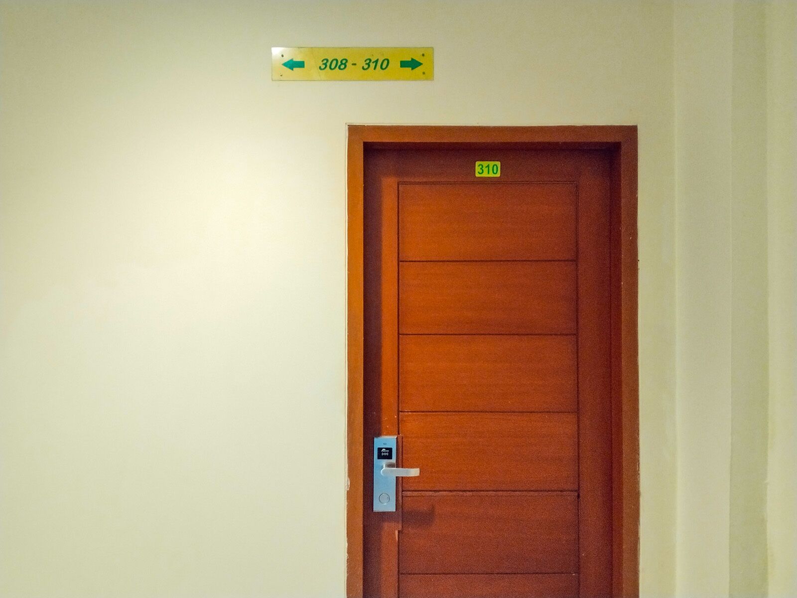 Una puerta de madera con una placa con el número 310, un timbre y un cartel que muestra los números de habitación 308 al 310.
