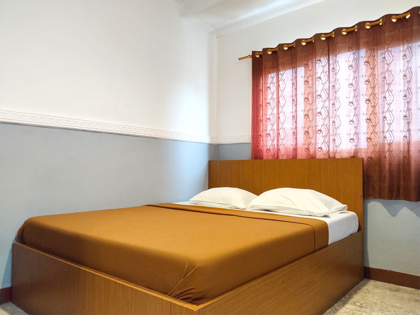 A single bed with a wooden headboard in a room with white walls and a red patterned curtain.