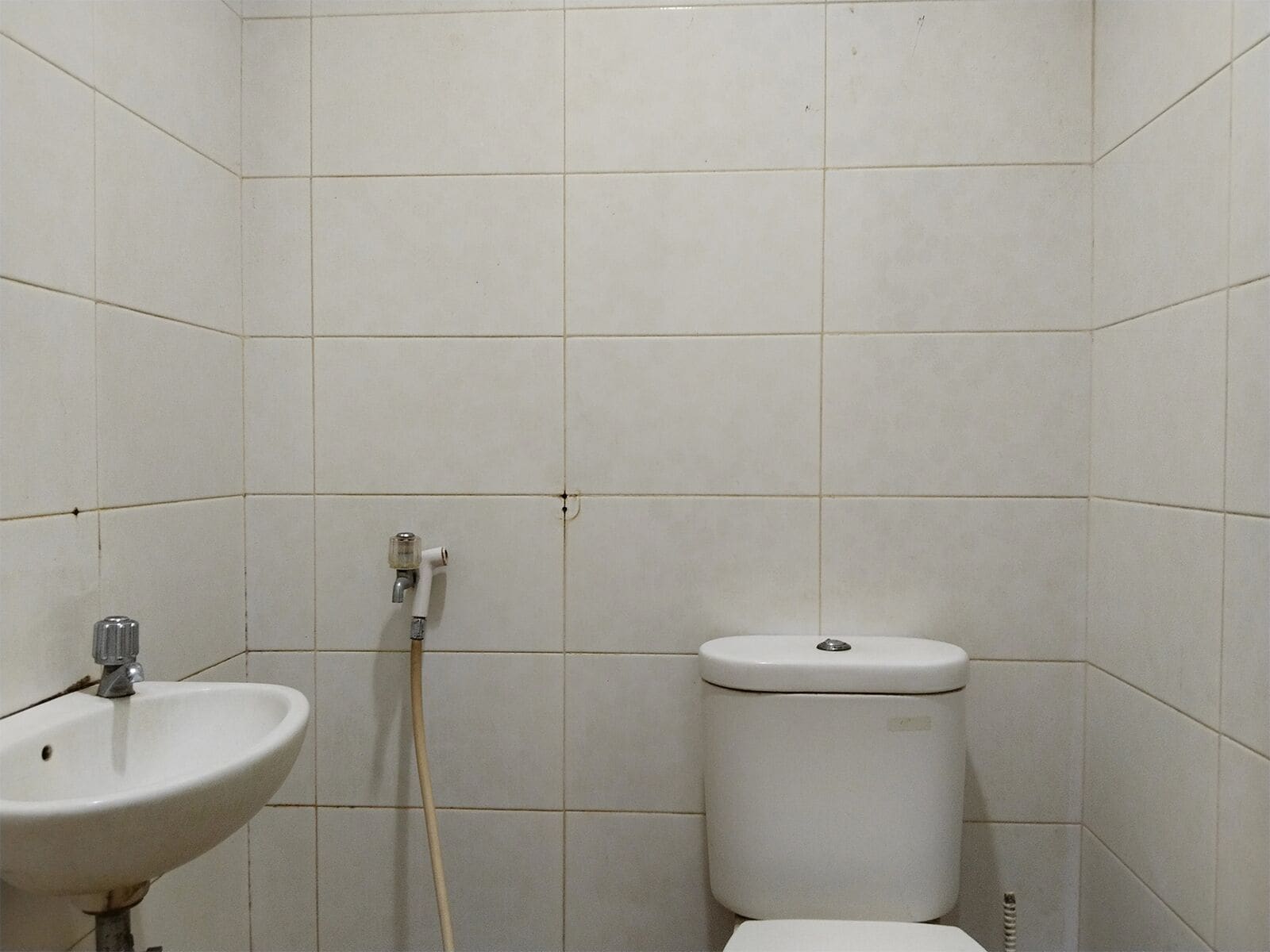 Un baño pequeño con paredes de azulejos, un lavamanos blanco y un inodoro.