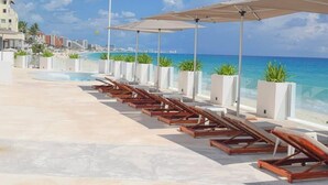Area piscina sulla spiaggia con lettini e ombrelloni, vista sull'oceano.