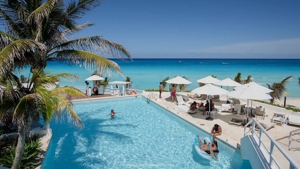Un'area piscina con acqua cristallina, sedie a sdraio, ombrelloni e palme.
