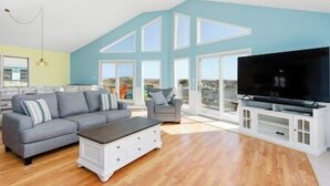 A spacious living room with a grey sofa, a white coffee table, and a flat-screen TV.