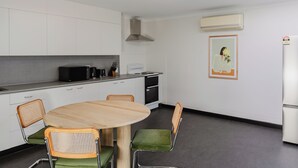 Een moderne keuken met witte kastjes, een ronde houten tafel, groene stoelen met kussens en een luchtverwarmer aan de muur.
