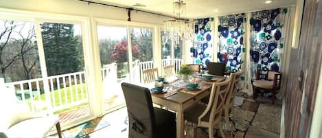 A dining area with a table set for four, surrounded by chairs, a chandelier, and a view of the outdoors.