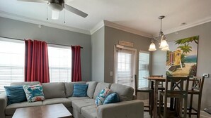 A living room with a sectional sofa, a coffee table, and a dining area with wooden chairs and a table. - Walk to the Beach- Peaceful and Modern Condo (Corpus Christi)