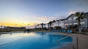 A swimming pool with a metal ladder, surrounded by lounge chairs and a row of multi-story buildings with balconies. - Walk to the Beach- Peaceful and Modern Condo (Corpus Christi)