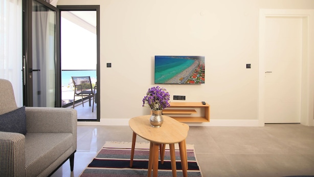 A modern living room with a sofa, a coffee table with a vase of flowers, a painting on the wall, and a sliding glass door leading to a balcony. - Krem Marin Suits Otel (Cesme)
