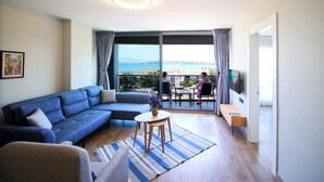 A modern living room with a sectional sofa, a small round table, and a view of the sea through large windows. - Krem Marin Suits Otel (Cesme)