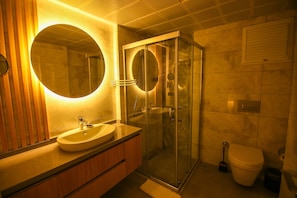 A modern bathroom with a round mirror, a sink, a glass-enclosed shower, and a toilet.