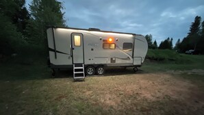 A recreational vehicle (RV) parked in a grassy area with a ladder leading to the door. - Cozy couples camper with your own private 100ft lake front.   (McMillan)