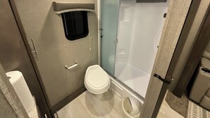 A compact bathroom with a toilet, a small window, and a shower area. - Cozy couples camper with your own private 100ft lake front.   (McMillan)