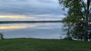 A grassy area with a calm lake and trees in the background. - Cozy couples camper with your own private 100ft lake front.   (McMillan)