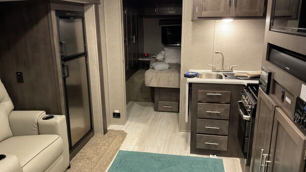 A compact RV kitchen with a refrigerator, stove, sink, and a small bed area. - Cozy couples camper with your own private 100ft lake front.   (McMillan)
