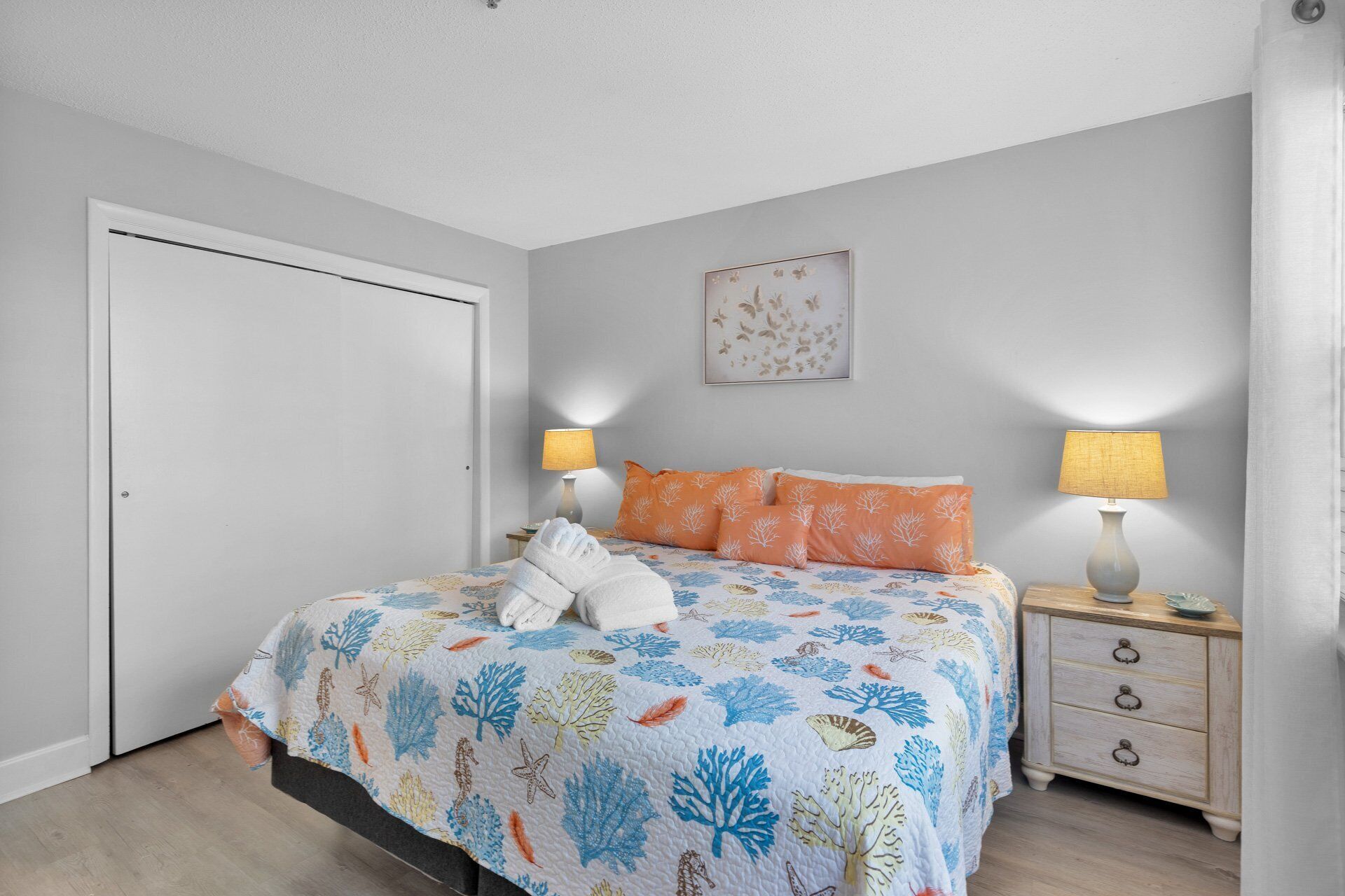 Une chambre à coucher avec un lit, deux lampes de chevet, une table de nuit, un tableau encadré au mur et une porte.
