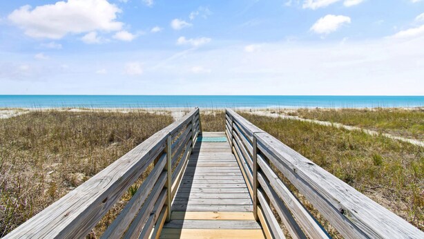 A wooden boardwalk leading to a beach with sand dunes and a clear blue sky. - "Lifesaver" is a 2 Bedroom, 1 Bathroom, Oceanfront Home! (Holden Beach)