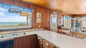 A wooden cabin with a kitchen featuring a sink, a dishwasher, and a dining area with white chairs and a table. - "Lifesaver" is a 2 Bedroom, 1 Bathroom, Oceanfront Home! (Holden Beach)
