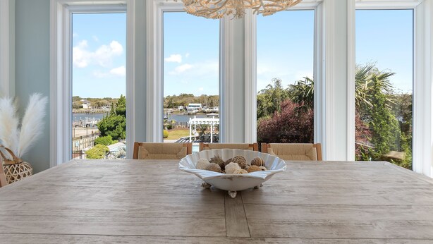 A dining area with a large table, a decorative bowl, and a view of a residential area through large windows.