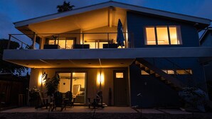 Een modern huis met twee verdiepingen, een balkon, buitenmeubilair en een trap.