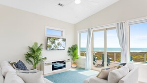Een ruime woonkamer met een grote televisie, comfortabele zitplaatsen, een open haard en een balkon met uitzicht op de oceaan.