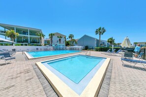 A pool area with two rectangular pools, lounge chairs, and palm trees.