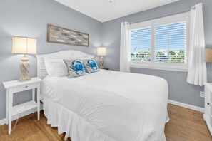 A bedroom with a bed, two bedside tables, a window with blinds, and a wall-mounted artwork.