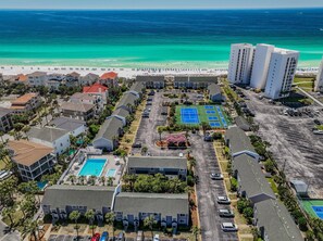 An aerial view of a coastal hotel with multiple buildings, a beach, and a tennis court.