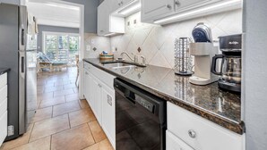 A modern kitchen with white cabinets, a granite countertop, a coffee maker, and a dishwasher. - Southbay by the Gulf 78, three hundred yards from the beach (Destin)