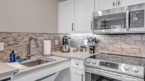 A modern kitchen with white cabinets, a stainless steel range, a microwave, and a tiled backsplash.