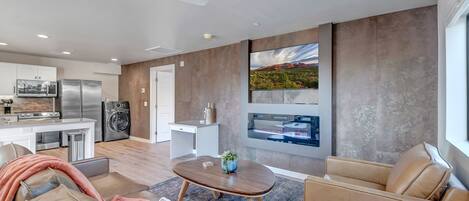 Una sala de estar moderna con sofá, sillones y una mesa de centro. Cuenta con una zona de cocina equipada y una mesa de comedor.