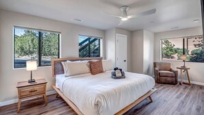 A modern bedroom with a large bed, a desk, a chair, and a ceiling fan.
