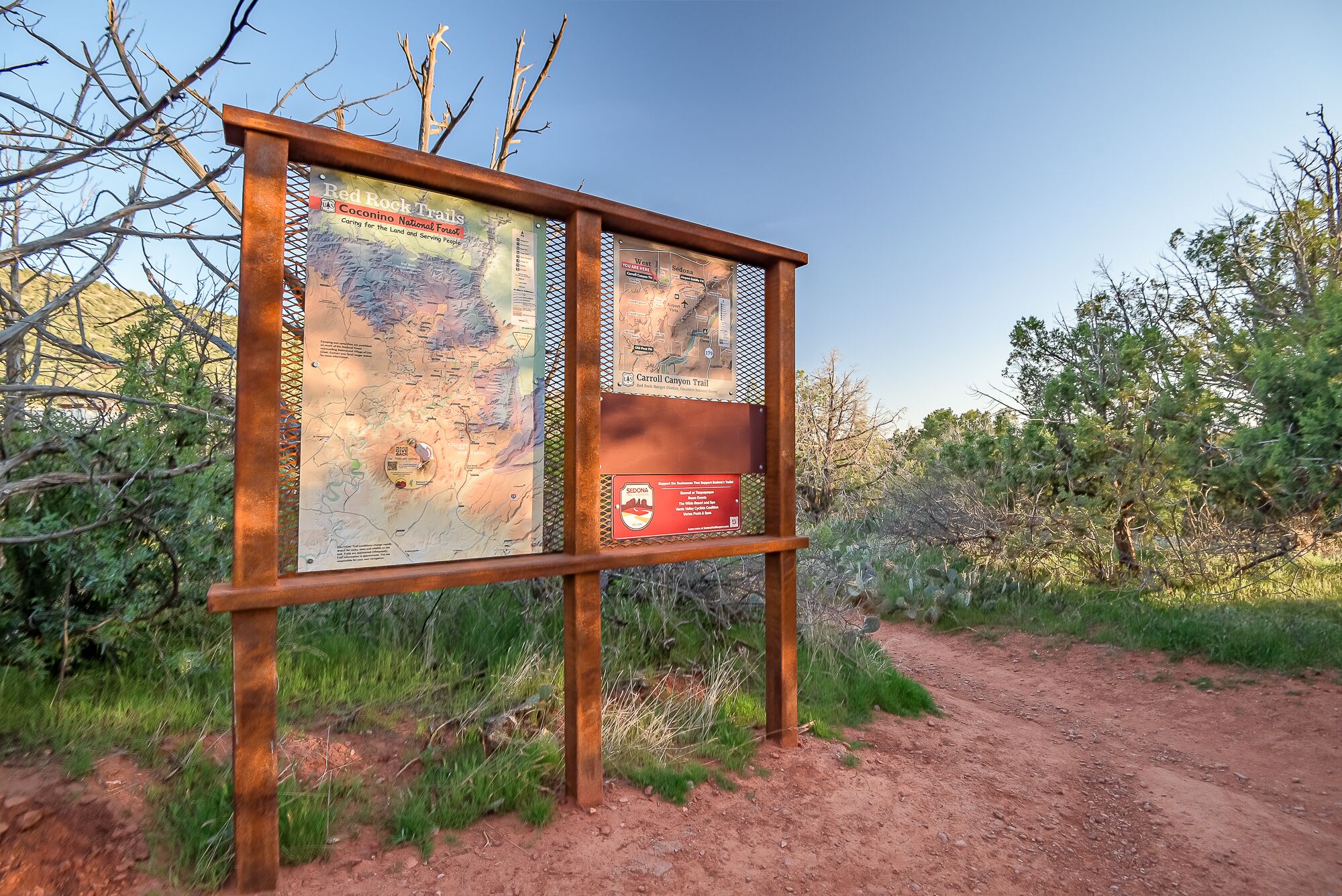 Un letrero metálico con mapas y texto, probablemente para una ruta o parque, sobre un fondo natural.