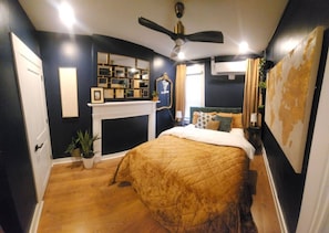 Um quarto com uma cama, lareira, ventoinha no teto e um mapa grande na parede.