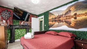 Une chambre à coucher avec un grand lit, un téléviseur à écran plat fixé au mur et un tableau représentant un paysage pittoresque au-dessus du lit.