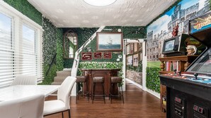 Une pièce avec une table et des chaises en bois, un escalier orné de plantes et des jeux d’arcade.